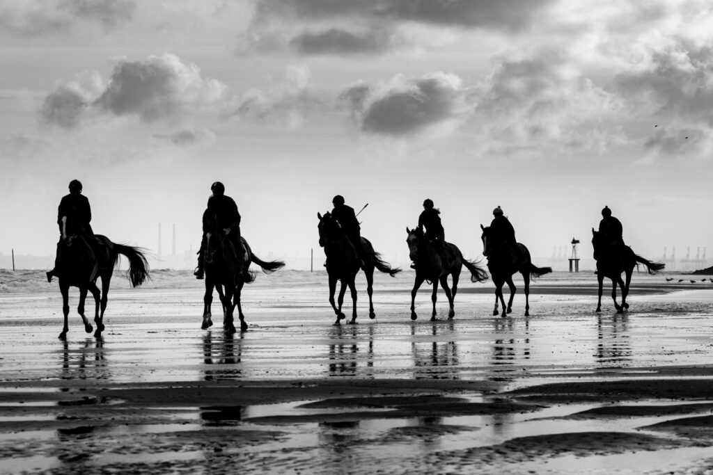 Silhouettes of jockeys riding horses on a reflective beach, symbolizing ARQANA's sonic branding identity crafted by Brandy Sound.