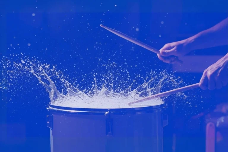 Drumsticks striking a drum with water splashing dramatically to illustrate the impact of sound marketing.